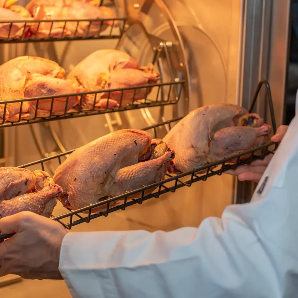 chicken being placed in a Fri-Jado Smart auto-clean rotisserie